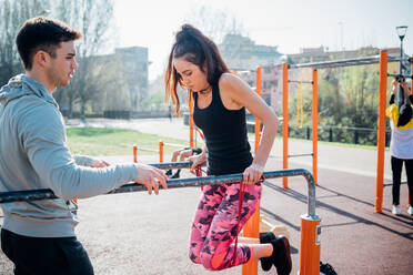 Calisthenics at outdoor gym, trainer watching young woman on parallel bars - CUF51976