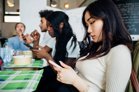 Ein männliches und ein weibliches Geschäftsteam schauen beim Arbeitsessen in einem Café auf ihre Smartphones, lizenzfreies Stockfoto