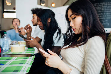 Ein männliches und ein weibliches Geschäftsteam schauen beim Arbeitsessen in einem Café auf ihre Smartphones - CUF51995