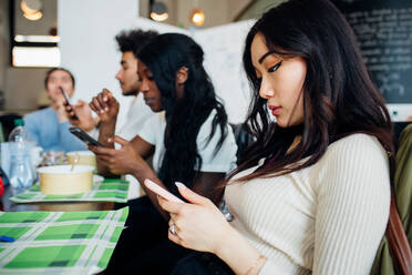 Male and female business team looking at smartphones while having working lunch at cafe table - CUF51995