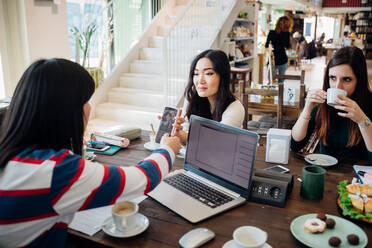 Female business team meeting while having working lunch at cafe table - CUF51997