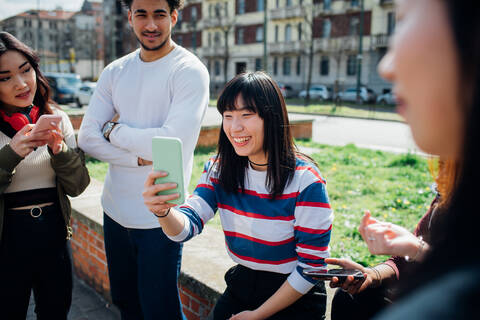 Junge weibliche und männliche erwachsene Freunde benutzen Smartphones in der Nähe einer Straße in der Stadt, lizenzfreies Stockfoto