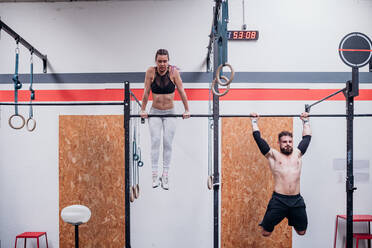 Junge Frau und Mann trainieren gemeinsam an Übungsstangen im Fitnessstudio - CUF52022