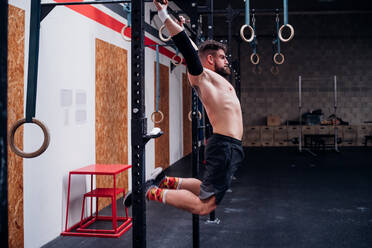 Junger Mann mit nacktem Oberkörper trainiert, schwingt an einer Stange im Fitnessstudio - CUF52024