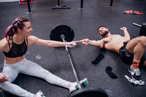 Junge Frau und Mann trainieren zusammen, berühren sich mit den Fingern über einer Langhantel im Fitnessstudio - CUF52028