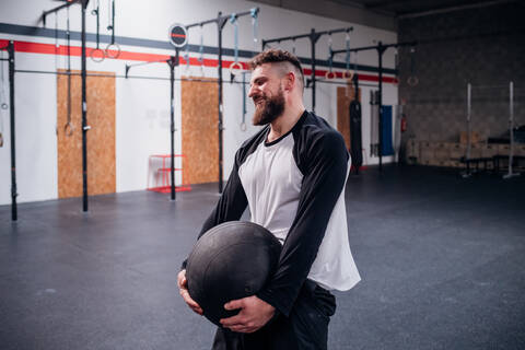 Junger Mann trainiert, hebt Atlaskugel im Fitnessstudio, lizenzfreies Stockfoto