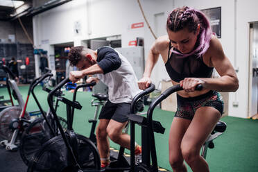 Junge Frau und Mann trainieren zusammen auf Heimtrainern im Fitnessstudio, Action - CUF52046