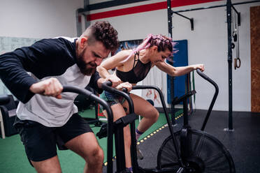 Junge Frau und Mann trainieren zusammen auf Heimtrainern im Fitnessstudio, Action - CUF52047