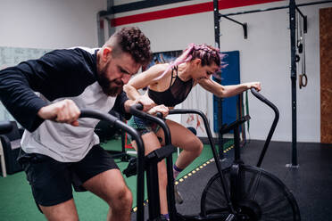 Young woman and man training together on gym exercise bikes, action - CUF52047