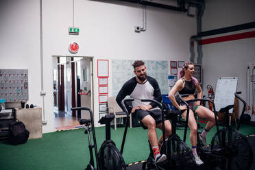 Exhausted young woman and man training together on gym exercise bikes, taking a break - CUF52048