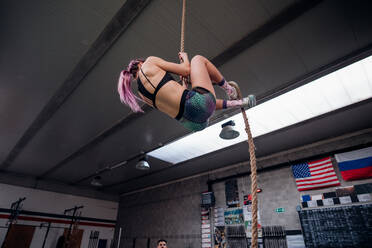Junge Frau trainiert, klettert an einem Übungsseil in einem Fitnessstudio hoch, niedriger Blickwinkel - CUF52052