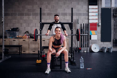 Junge Frau und Mann trainieren zusammen im Fitnessstudio, sitzen auf der Hantelbank, Porträt - CUF52062