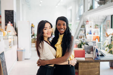 Young businesswomen hugging in bookshop, portrait - CUF52063