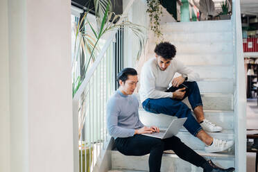 Young businessmen sitting on stairway using laptop - CUF52064