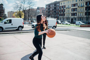 Young female friends playing basketball on city court - CUF52067