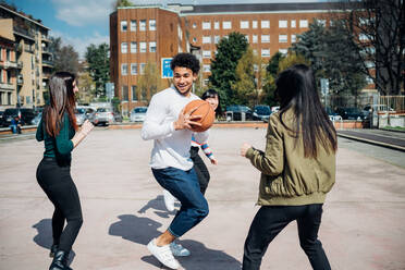 Young female and male adult friends playing basketball on city court - CUF52069