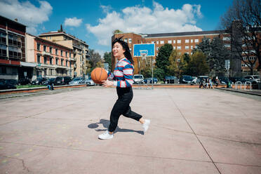 Young woman playing basketball on city basketball court - CUF52073