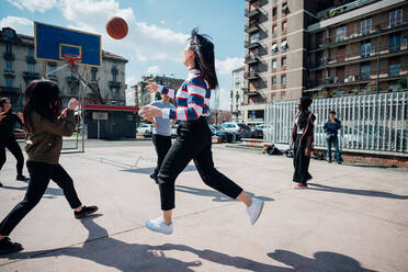 Young female and male adult friends playing basketball on city basketball court - CUF52074