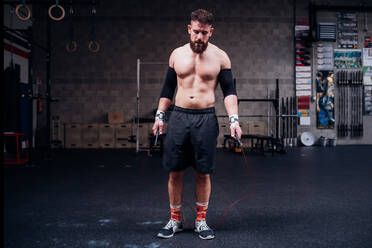 Junger Mann mit nacktem Oberkörper trainiert, hält Springseil im Fitnessstudio - CUF52083