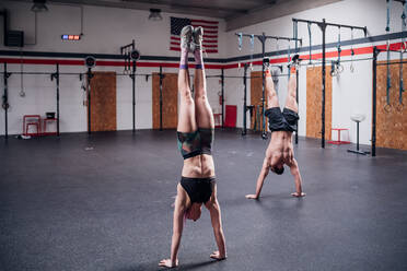 Junge Frau und Mann trainieren zusammen, machen Handstand im Fitnessstudio - CUF52087