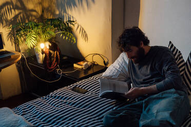 Bärtiger junger Mann liest Buch im Bett - CUF52118