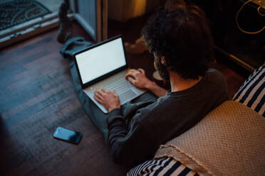 Bärtiger junger Mann benutzt Laptop im Schlafzimmer - CUF52129