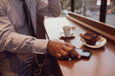 Businessman using smartphone at tea time in cafe - CUF52169