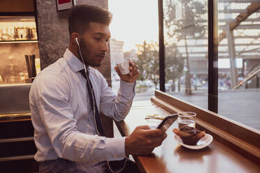 Businessman using smartphone at tea time in cafe - CUF52170