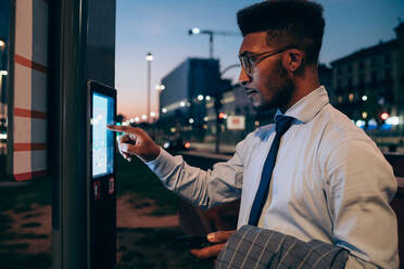 Geschäftsmann, der ein digitales Informationssystem an einer Bushaltestelle benutzt, Mailand, Lombardei, Italien - CUF52190