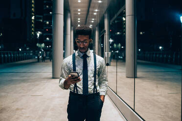 Businessman using smartphone, walking past mirrored wall of office building, Milano, Lombardia, Italy - CUF52197