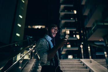 Businessman using smartphone on stairs of office building - CUF52207