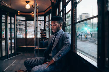 Businessman using smartphone on tram in city - CUF52234