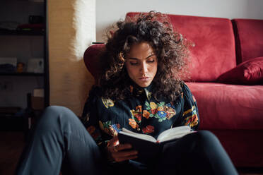 Frau liest ein Buch und lehnt sich an ein Sofa - CUF52258
