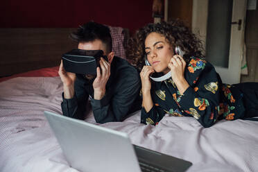 Couple using VR headset and laptop on bed - CUF52271