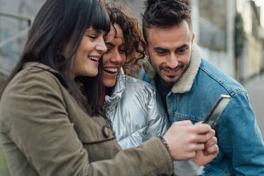 Friends using smartphone on pavement - CUF52288