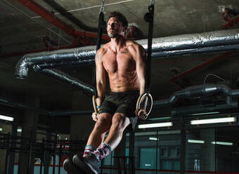 Mann trainiert mit Gymnastikringen in einer Turnhalle - CUF52401