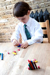 Junge in Schuluniform spielt zu Hause mit Farbstiften - CUF52440