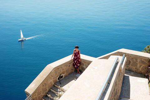 Junge Frau genießt sonnigen Tag am Meer, Segelboot im Hintergrund, Alghero, Sardinien, Italien, lizenzfreies Stockfoto