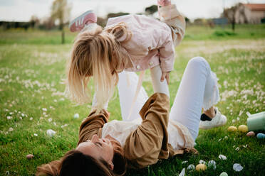 Mother lying on back holding up daughter in wildflower field after easter egg hunt, Arezzo, Tuscany, Italy - CUF52471