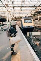 Woman waiting on platform in train station, Edinburgh, Scotland - CUF52495