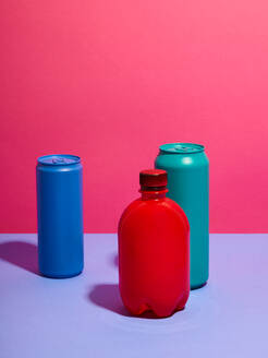 Stilleben aus türkisfarbenen und blauen Getränkedosen mit roter Flasche und rosa Hintergrund - CUF52534