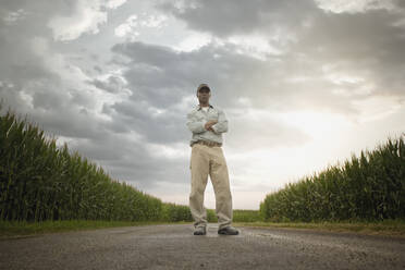 Ein afroamerikanischer Landwirt steht auf einer Straße zwischen Feldern - BLEF07861