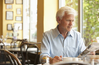 Caucasian man reading newspaper in restaurant - BLEF07894