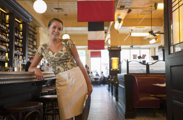 Caucasian waitress leaning on bar in restaurant - BLEF07899