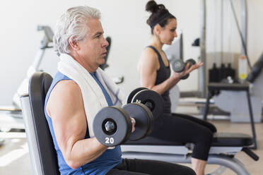 Older Hispanic man lifting weights in gym - BLEF08036