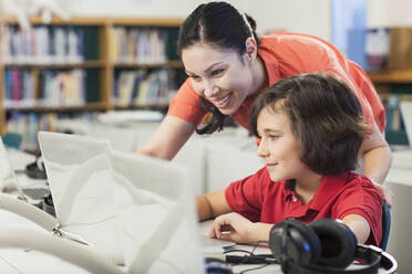 Lehrerin und Schülerin benutzen Laptop in der Bibliothek - BLEF08059