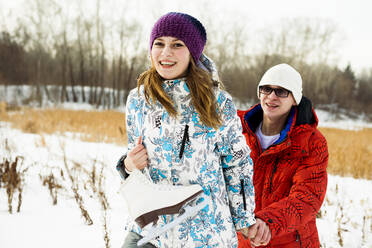 Caucasian couple carrying ice skates in snowy field - BLEF08110