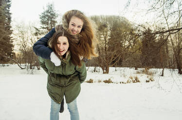 Caucasian woman carrying friend piggyback in snowy field - BLEF08120