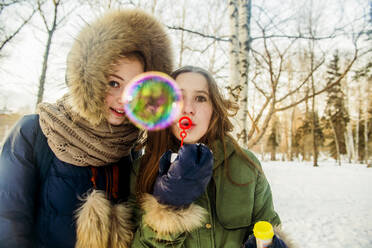 Caucasian women blowing bubbles in snowy field - BLEF08122