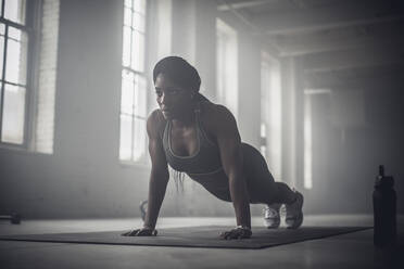 Black woman doing push-ups in dark gym stock photo